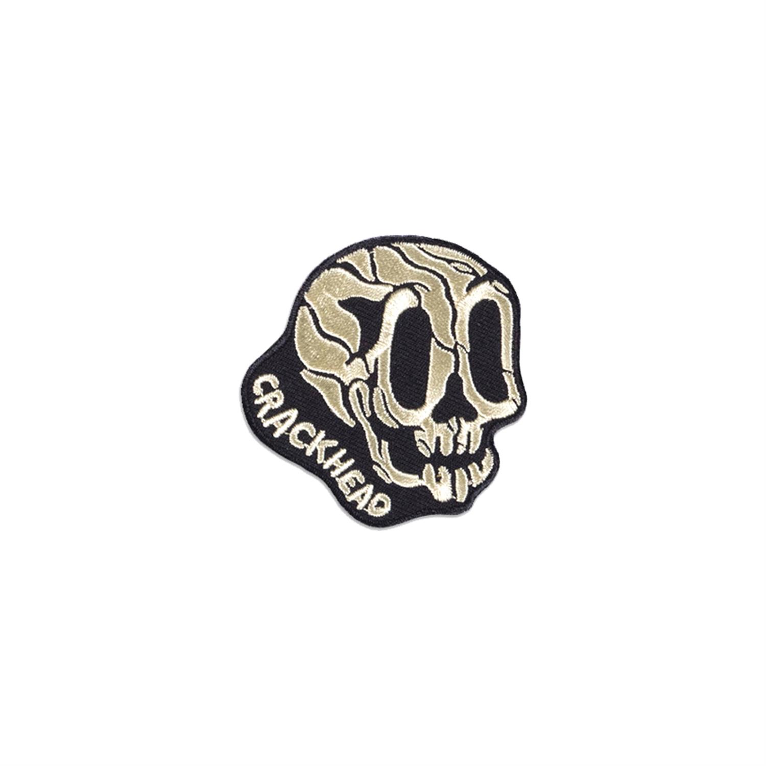 Ein gestickter Aufnäher in Form eines Totenkopfs mit dem Schriftzug 'Crackhead'. Er ist schwarz und beige.